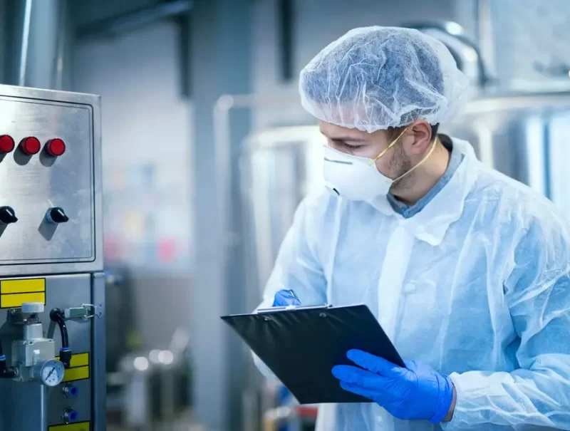 technologist-expert-protective-uniform-with-hairnet-mask-taking-parameters-from-industrial-machine-food-production-plant_342744-1176